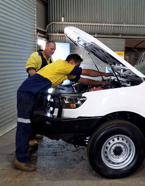 Trainee in automotive leaning over open bonnet