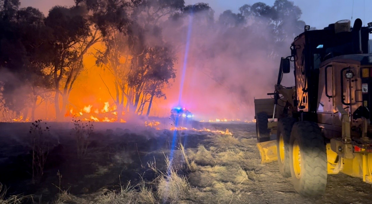 Fire in Bush Land with a council Grader and an emergency Services vehicle in the background